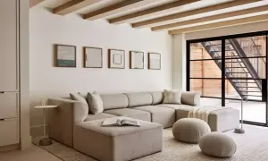 Przytulny salon z dużą, beżową sofą i pufami. Dominują tu **kolory pastelowe**, tworząc spokojną atmosferę.
