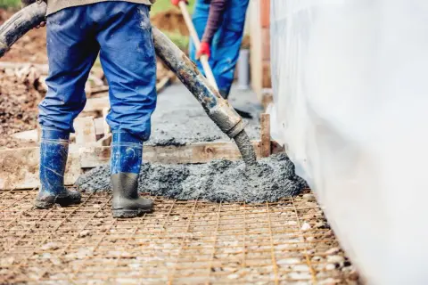 Robotnicy wylewają beton na zbrojenie. Waga betonu jest kluczowa dla wytrzymałości konstrukcji.