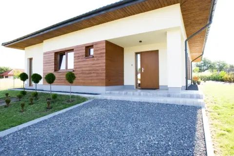 Nowoczesny dom z jasnym tynkiem, drewnianą elewacją imitującą tynk kornik i brązowymi oknami.