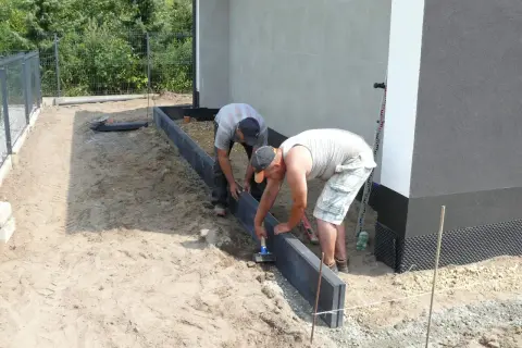 Dwóch mężczyzn układa obrzeża. Prawidłowe suchy beton proporcje są kluczowe dla trwałości.