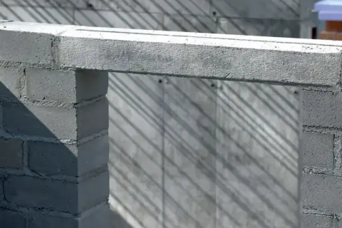 Betonowy nadproże nad otworem w budowie, podparty na bloczkach. Cienie na ścianie tworzą ciekawy wzór.