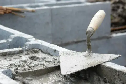 Łopata z zaprawą na budowie ogrodzenia murowanego tynkowanego.