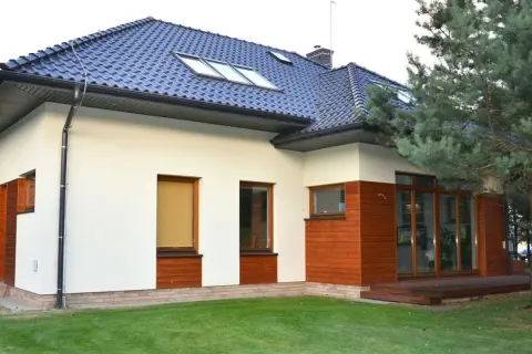 Nowoczesna **struktura elewacyjna** domu z białym tynkiem, drewnianymi panelami i dużymi oknami.