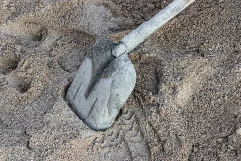 Łopata w piasku, ślady butów i opon. Przygotowanie do budowy, kluczowe są chudy beton proporcje.