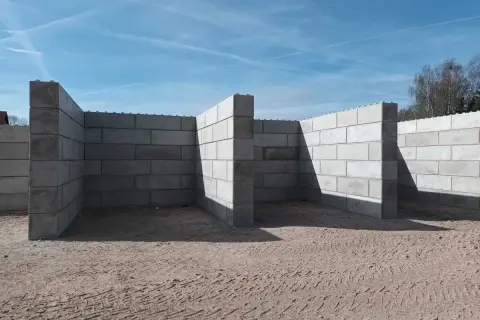 Budowa muru oporowego z bloczków betonowych. Konstrukcja w kształcie litery L, z widocznymi słupkami wzmacniającymi.