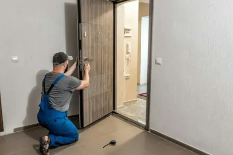 Monter w niebieskich ogrodniczkach montuje drzwi zewnętrzne, klamiąc klamkę.