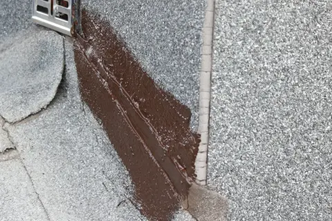 Brązowy lepik uszczelnia dach. Widać metalowy element odpływu.