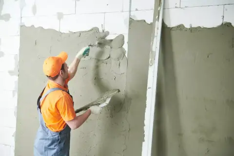 Budowlaniec nakłada tynki wapienne na ścianę z bloczków.