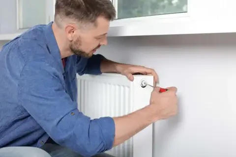 Mężczyzna odpowietrza grzejnik, próbując rozwiązać problem, dlaczego grzejnik jest zimny na dole.