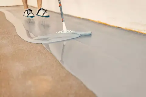 Osoba w butach rozlewa szarą żywicę, tworząc gładkie podłogi epoksydowe.