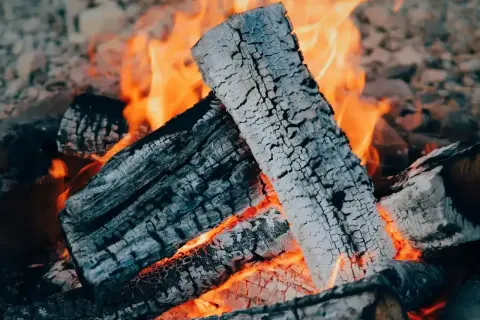Płonące polana, z których unosi się biały **popiół**, tworzą ciepły, pomarańczowy blask.