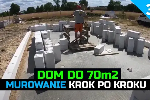 Budowa domu 70m2: murowanie ścian z bloczków betonowych. W tle plac budowy i pracownik.