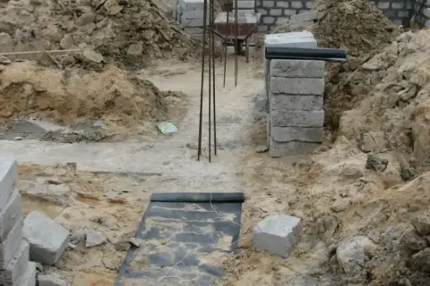 Budowa domu w toku: zbrojenie, bloczki betonowe i ziemia tworzą fundamenty.