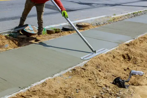 Robotnik wygładza świeży beton B25, dbając o właściwe proporcje mieszanki do budowy chodnika.