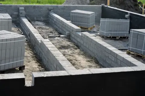 Budowa fundamentów z bloczków betonowych, przygotowanie pod ocieplenie fundamentów. Materiały budowlane czekają na użycie.