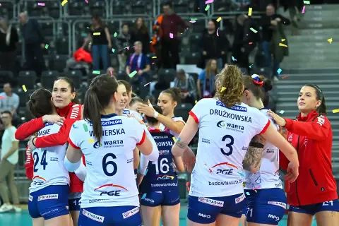 Siatkarki w strojach sportowych przytulają się, obsypane konfetti.