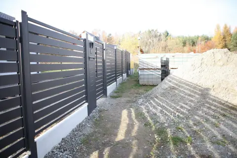 Solidny fundament pod bramę przesuwną, gotowy na montaż nowoczesnego ogrodzenia. Obok materiały budowlane.