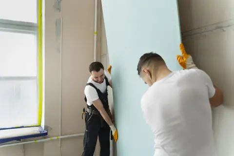 Dwóch mężczyzn montuje płyty gipsowe, przygotowując je do szpachlowania łączeń.