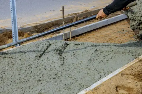 Prace budowlane: świeży beton, który będzie miał fakturę betonu szczotkowanego, jest rozkładany łopatą.