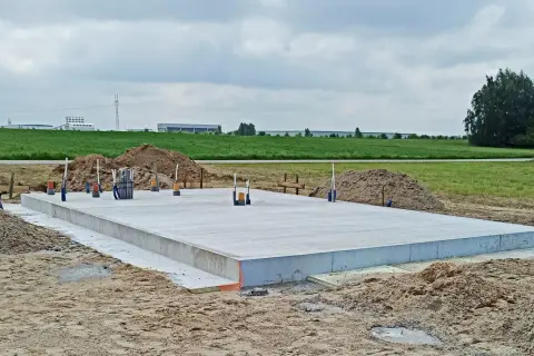 Solidna płyta fundamentowa na budowie, otoczona piaskiem i zielenią.