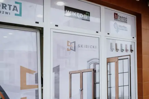 Witryna sklepowa z logo firm okiennych i drzwiowych oraz zdjęciami produktów.