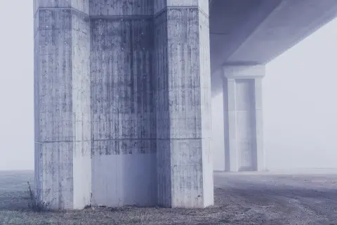 Monumentalne filary mostu, prezentujące różne klasy ekspozycji betonu, toną we mgle.